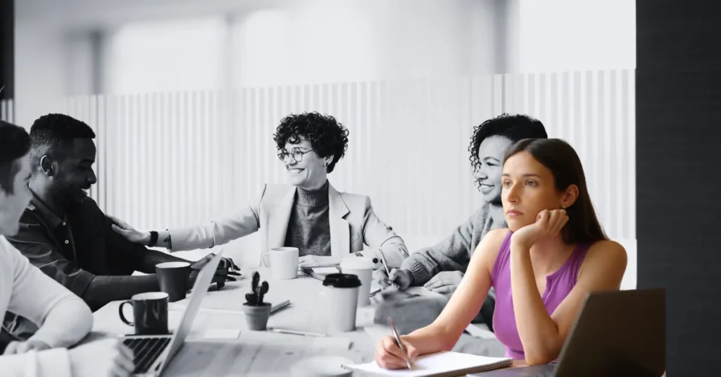 Grupo de personas atendiendo una reunión de trabajo, pero una de ellos está en actitud ausente y distante.