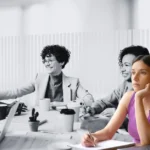 Grupo de personas atendiendo una reunión de trabajo, pero una de ellos está en actitud ausente y distante.