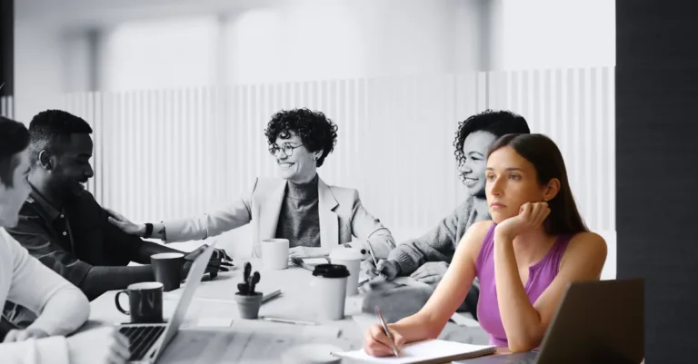 Grupo de personas atendiendo una reunión de trabajo, pero una de ellos está en actitud ausente y distante.