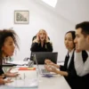 Personas reunidas en junta de trabajo, discutiendo. Ambiente tenso.