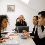 Personas reunidas en junta de trabajo, discutiendo. Ambiente tenso.