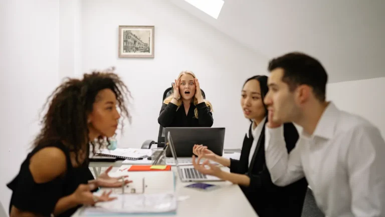 Personas reunidas en junta de trabajo, discutiendo. Ambiente tenso.